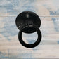 Black forged iron barn dome cabinet pull with a circular ring and rustic finish, mounted on a light wooden background.