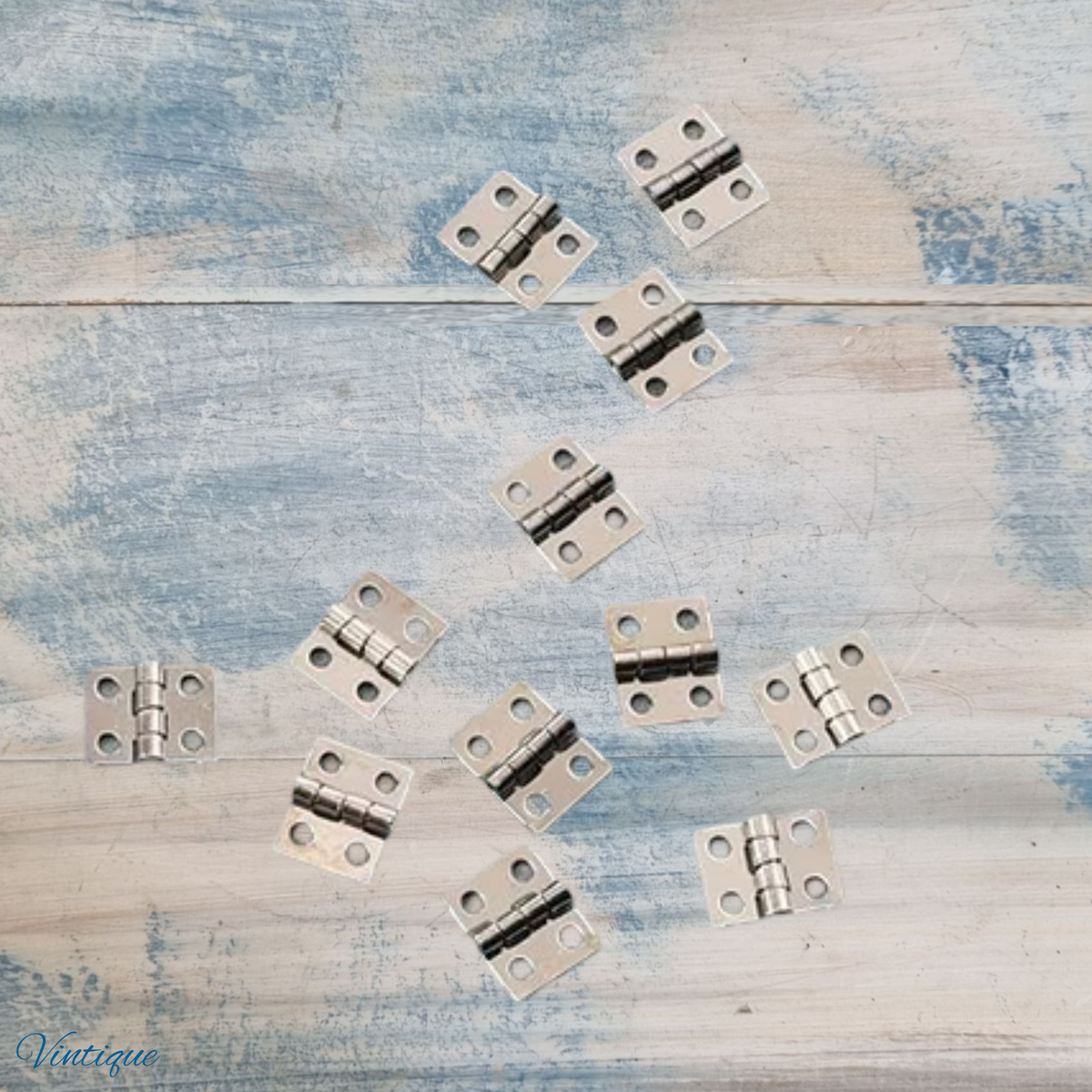 small silver metal cabinet hinges arranged on a distressed blue and white wooden surface.