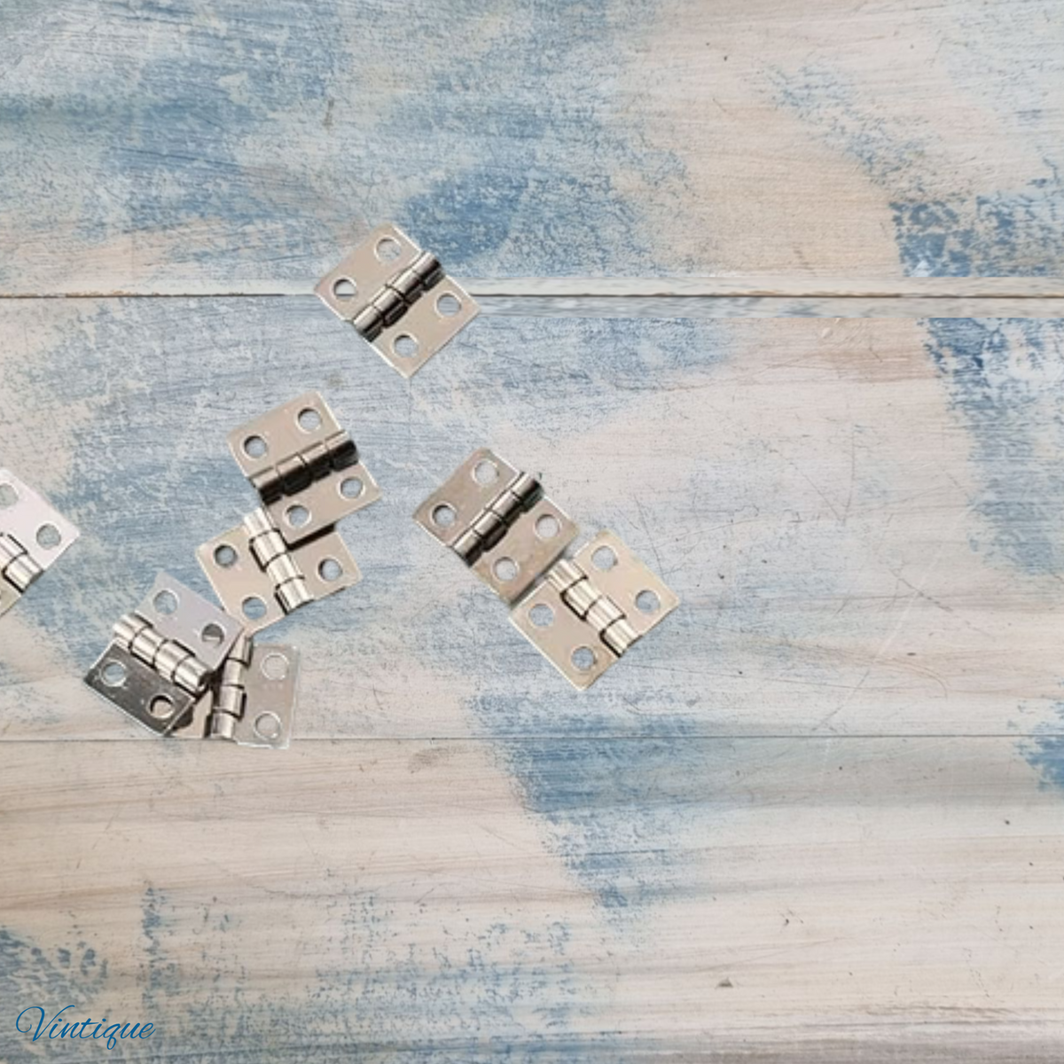 Several small silver metal cabinet hinges scattered on a distressed blue and white wooden surface.