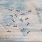 Ten small metal hardware pieces with two round holes, arranged on a distressed blue and white wooden surface. A 'Vintique' brand watermark is visible in the bottom-left corner.