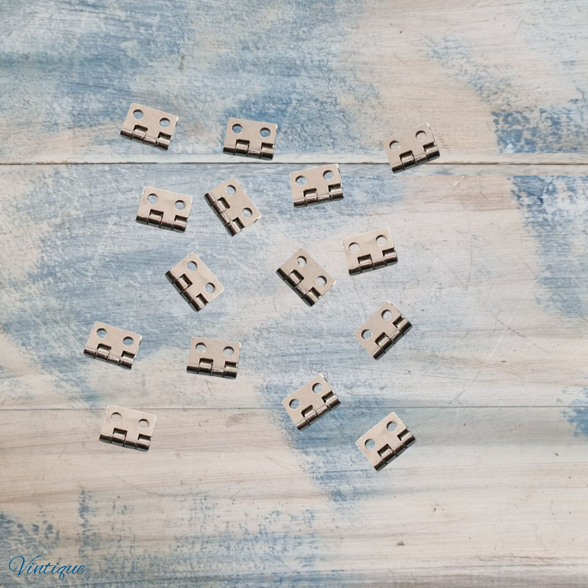 Ten small metal hardware pieces with two round holes, arranged on a distressed blue and white wooden surface. A 'Vintique' brand watermark is visible in the bottom-left corner.