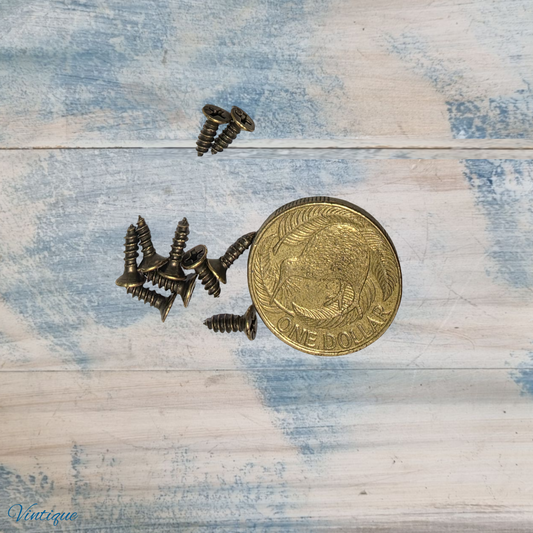 Ten bronze wood screws scattered around a one dollar coin on a light wooden surface.