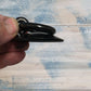 Black forged iron ring pull held between fingers, featuring a rustic design and a smooth finish