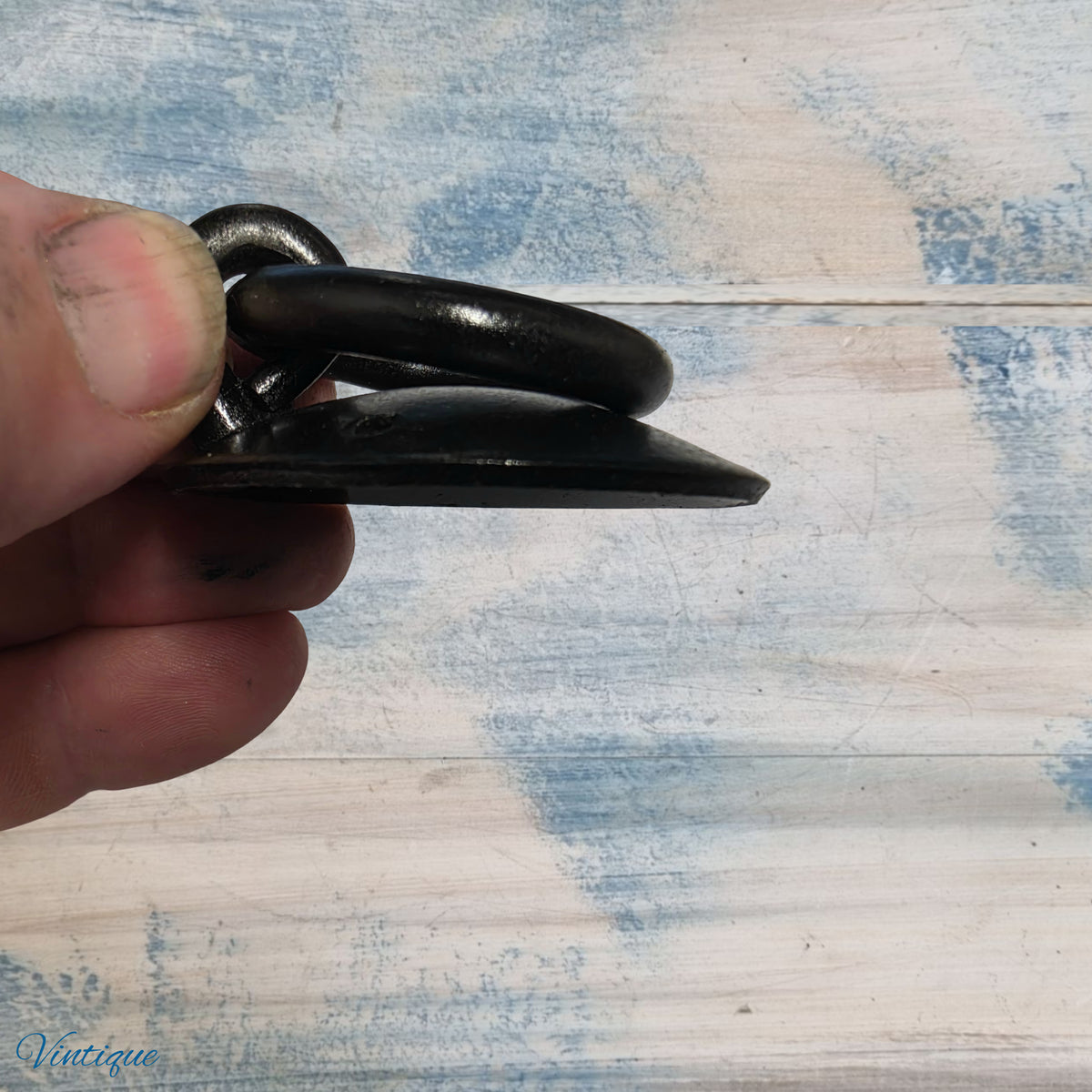 Black forged iron ring pull held between fingers, featuring a rustic design and a smooth finish