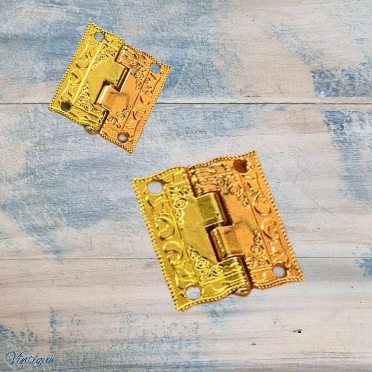 Two ornate gold-toned decorative hinges with embossed floral scrollwork