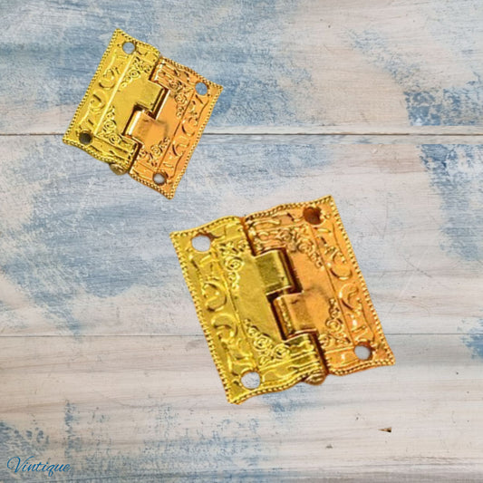 Two ornate gold-toned decorative hinges with embossed floral scrollwork